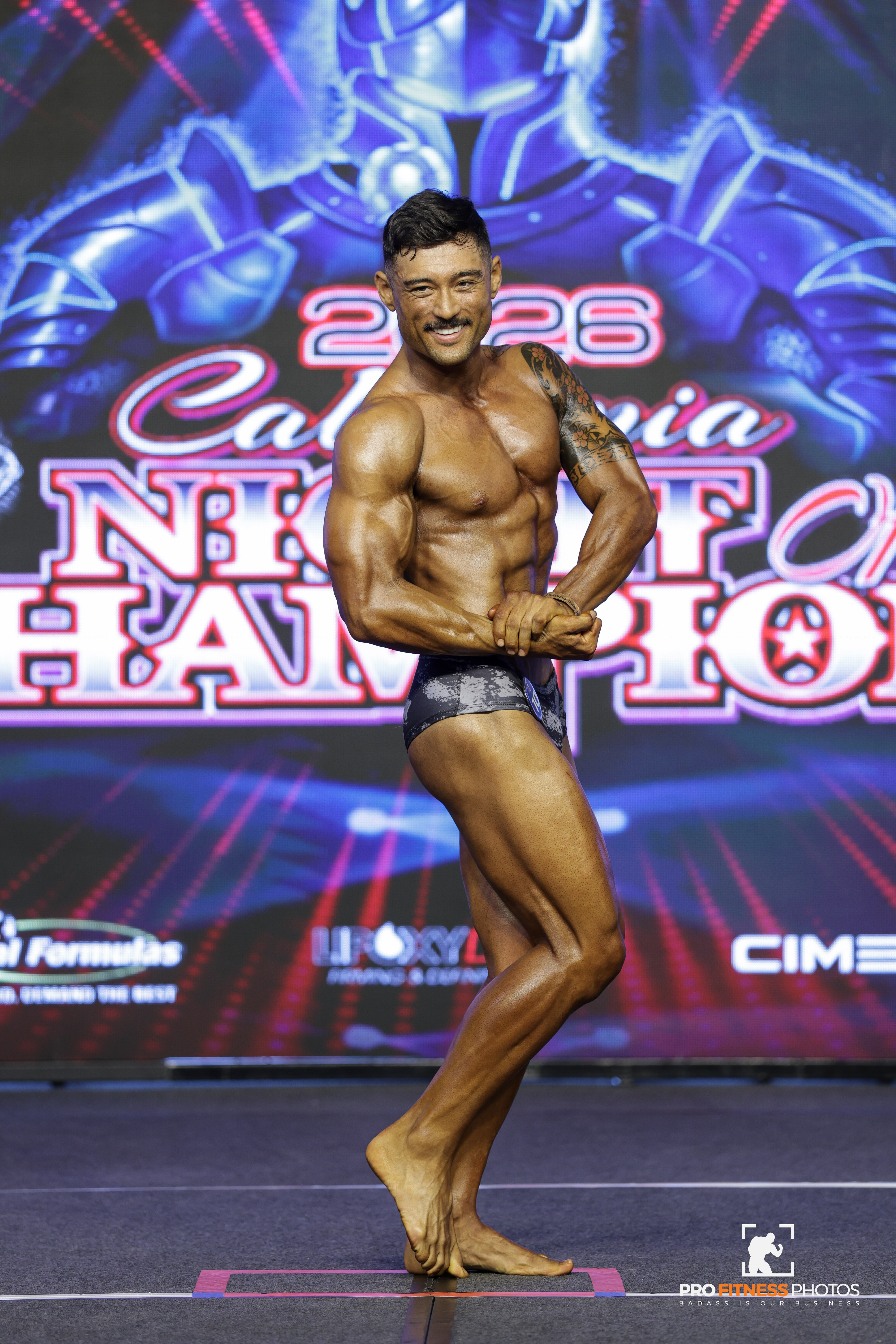 Tyler Murata competing on stage in a side-chest pose